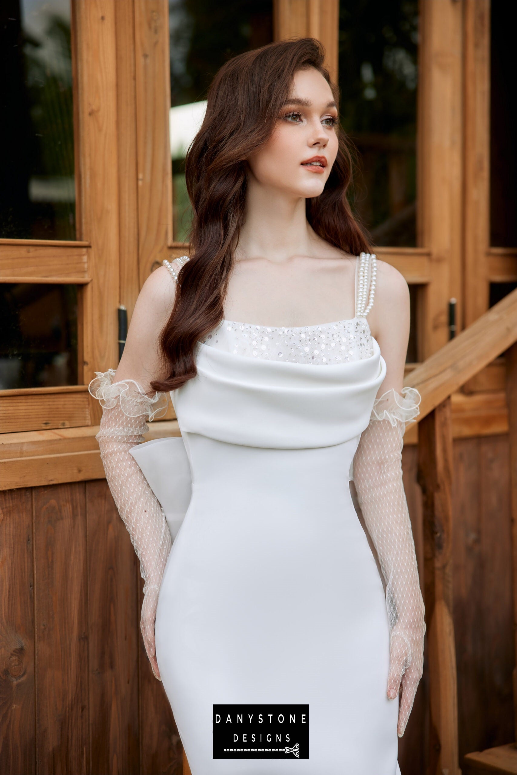 Bride wearing a satin neckline wedding dress with pearl strap back, standing by a wooden window