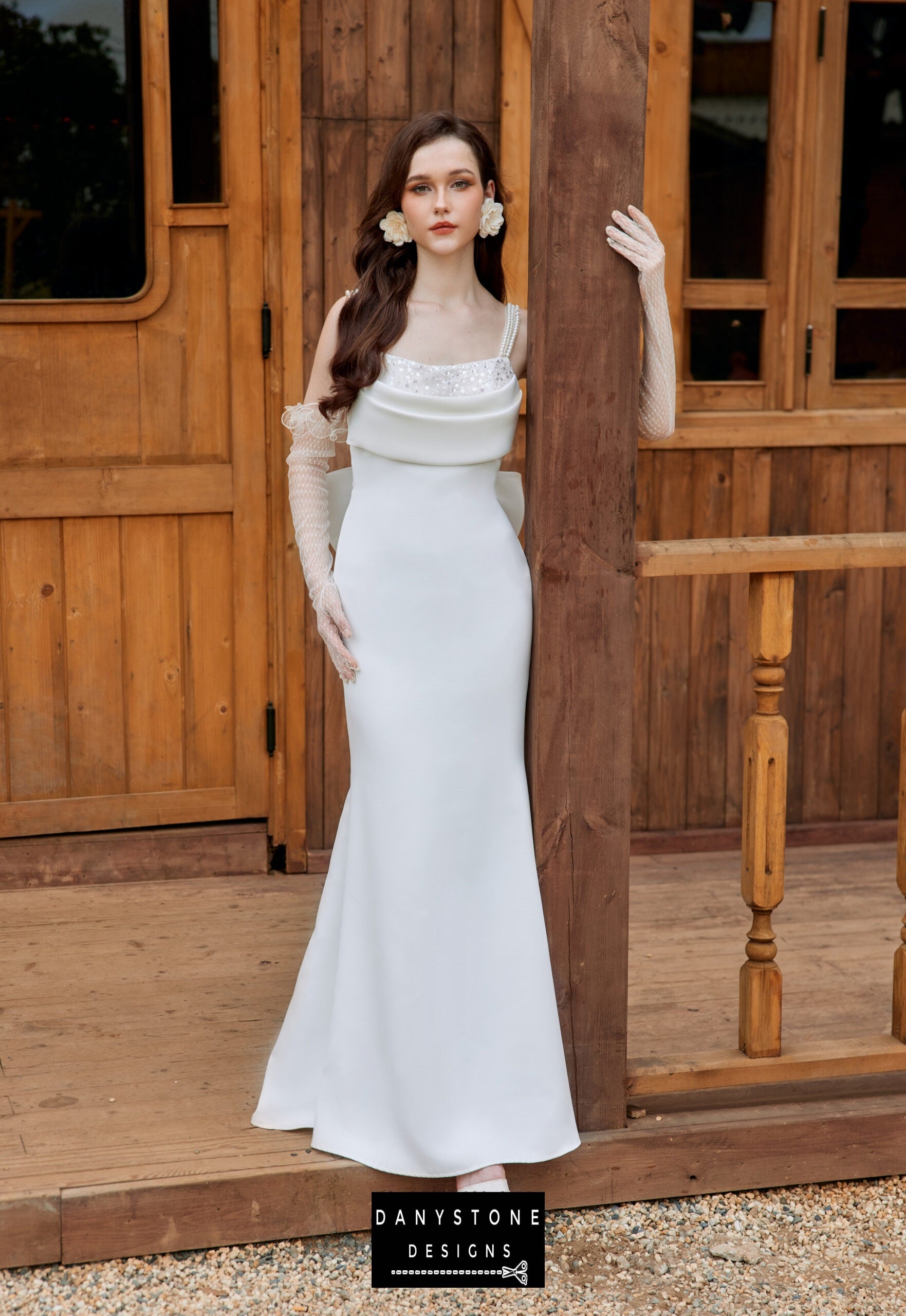 Bride in a satin neckline wedding dress with pearl strap back, leaning against a wooden pillar.