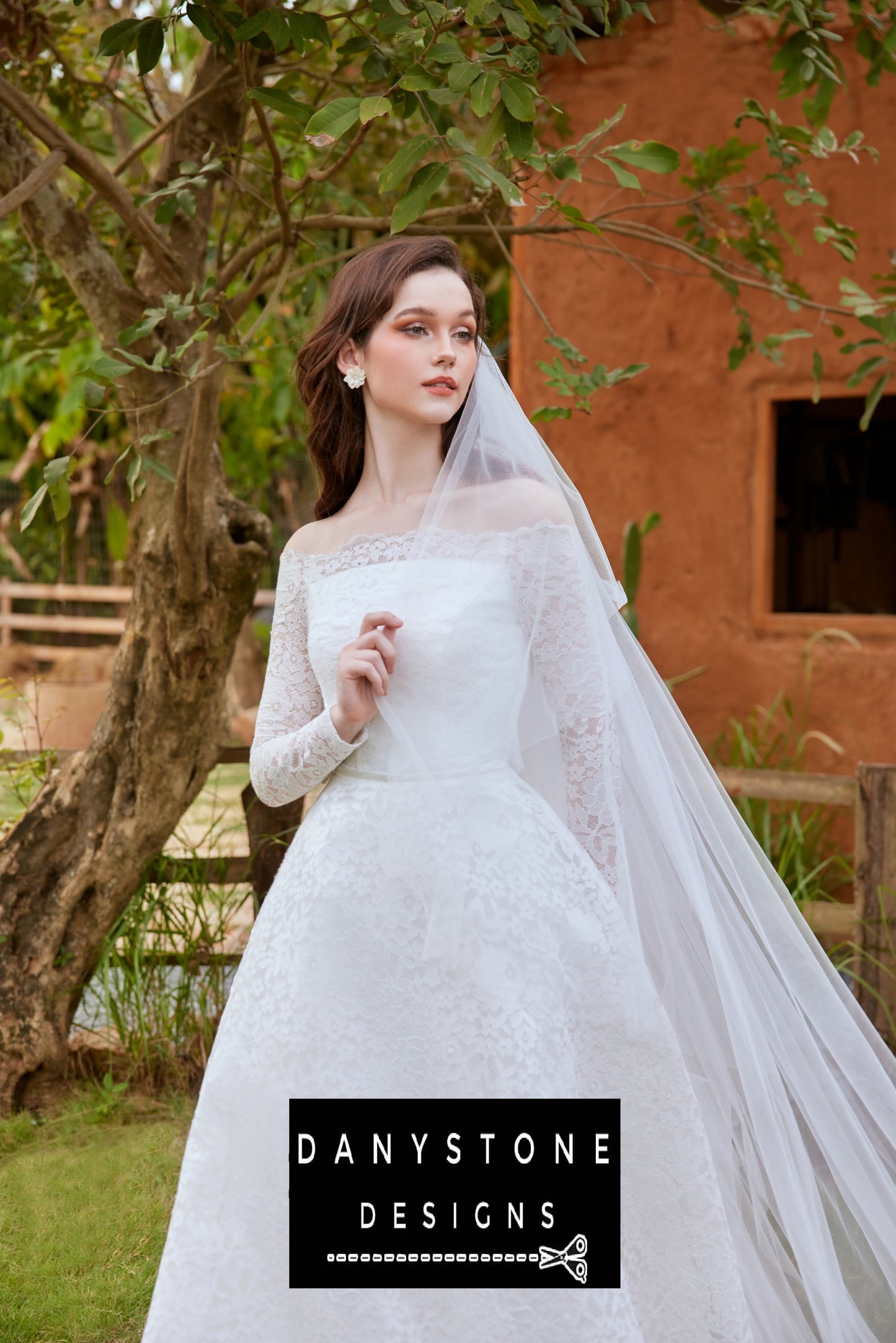 Bride posing under a tree, wearing a lace wedding dress with puffed shoulders and a long veil.