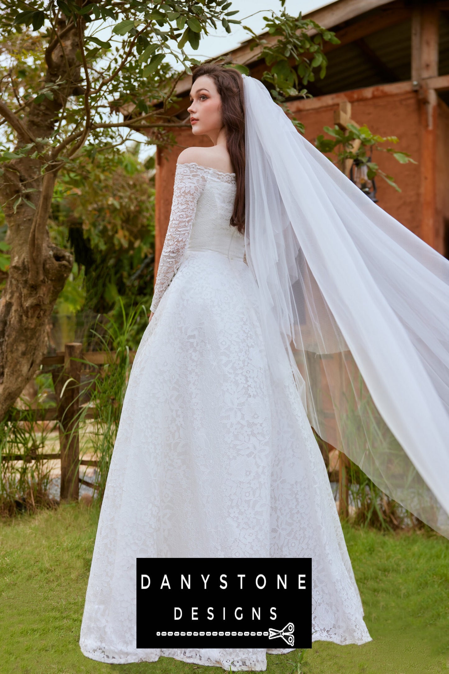 Back view of the bride in a lace wedding dress with puffed shoulders, showing the full-length skirt and veil flowing in the breeze.