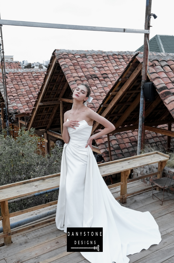 Full-Length Pleated Strapless Gown - Model posing in the full-length pleated strapless gown with a romantic and ethereal skirt.