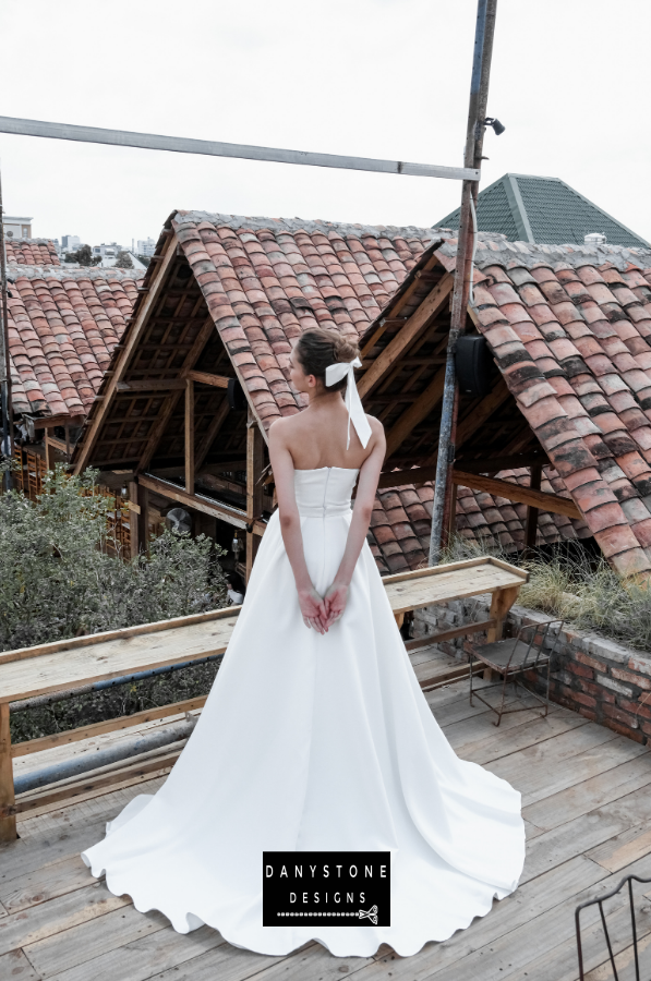 Graceful Pleated Strapless Gown - Back view of the model with the flowing skirt and elegant pleats, perfect for a timeless bridal look.