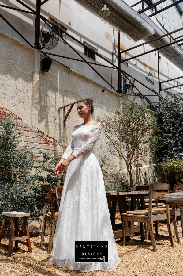 Model posing in an outdoor setting wearing the thin lace dress with off-shoulder design.