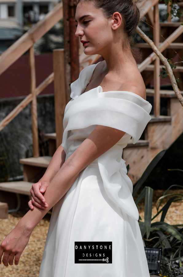 Classic Off-the-Shoulder Bridal Dress with Bow Detail - Model presenting the side view of the gown, showcasing the elegant pleats and captivating bow at the back.