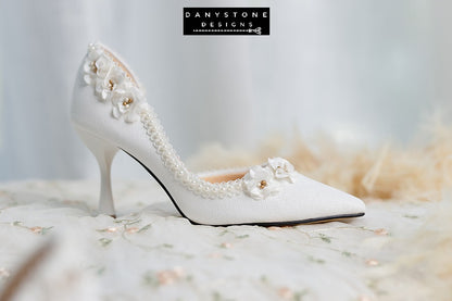 Elegant wedding shoes with open waist, pearl trim, and floral accents, displayed on a white fur background.