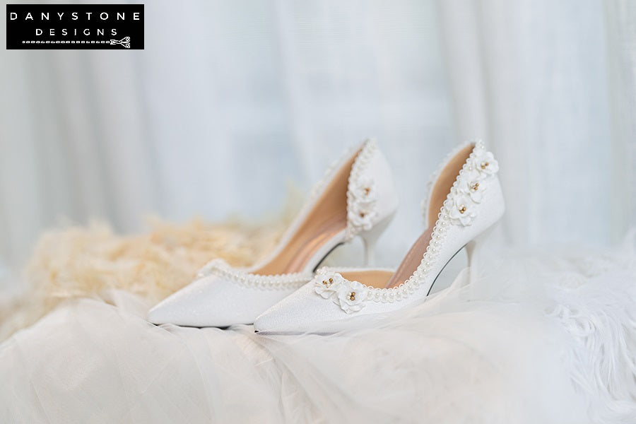 Pair of wedding shoes with open waist, pearl trim, and floral accents, perfect for brides.