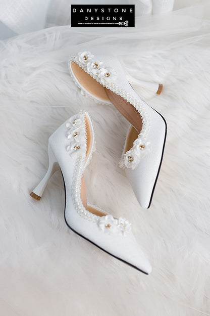 Close-up of wedding shoes with open waist, pearl trim, and floral accents, highlighting intricate details.