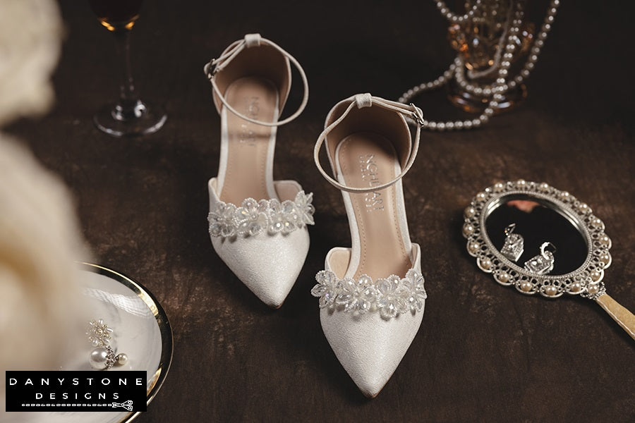 Elegant bridal heels with crystal beaded floral design, displayed with pearl and mirror accessories.