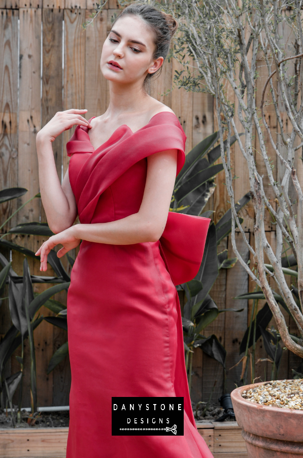 Chic red silk evening dress with a flowing mermaid silhouette, featured in an outdoor garden setting.