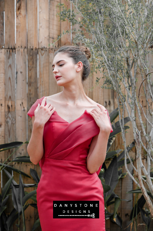 Sophisticated red gown with a fitted bodice and pleated mermaid tail, showcased in a serene outdoor environment.