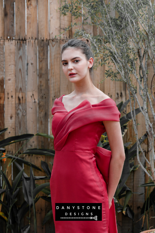 Elegant woman posing in a red mermaid gown with pleated details, set against a natural garden backdrop