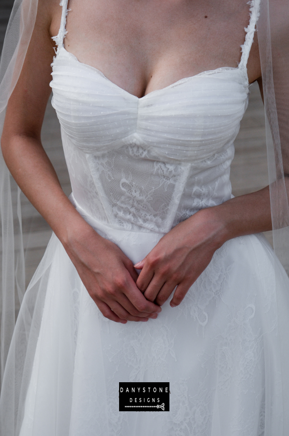 Bride in full corset lace dress with bustier bust and tulle overlay, side profile.