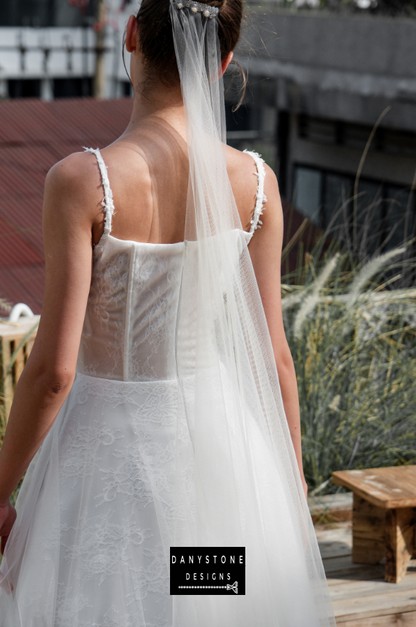 Bride in full corset lace dress with bustier bust and tulle overlay, side view.