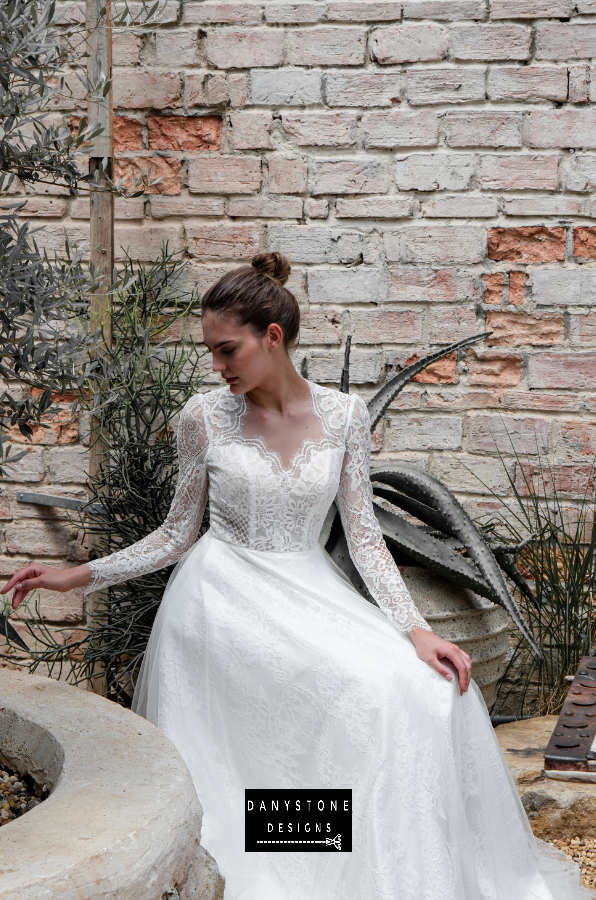 Model sitting and showcasing the long lace sleeves and intricate design of the dress.