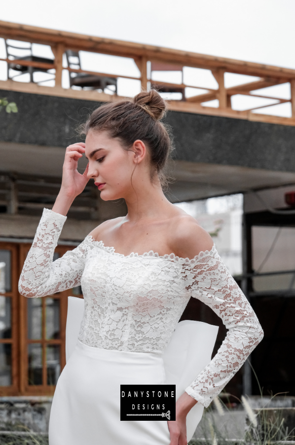 Model posing in a sophisticated setting wearing the satin fishtail flat shoulder dress.