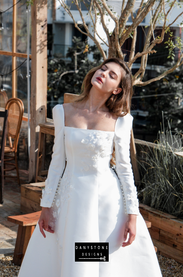  Model posing in an outdoor setting wearing the 7-piece tafta dress with embossed flowers and long sleeves.