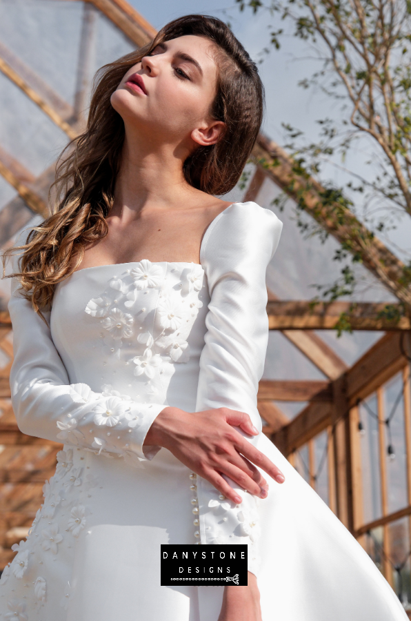 Model posing in an outdoor setting wearing the 7-piece tafta dress with embossed flowers and long sleeves.