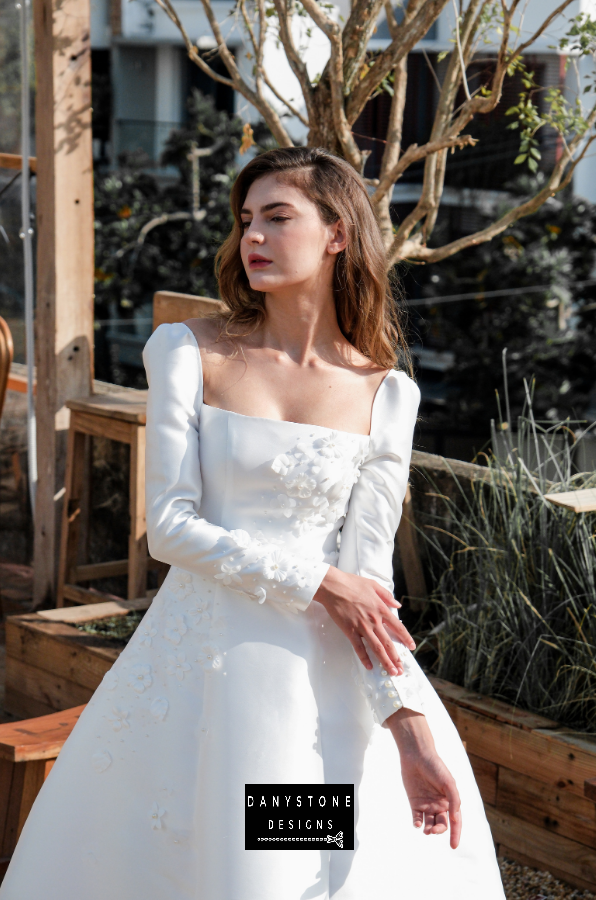 Model posing in a greenhouse setting wearing the 7-piece tafta dress with embossed flowers and long sleeves.