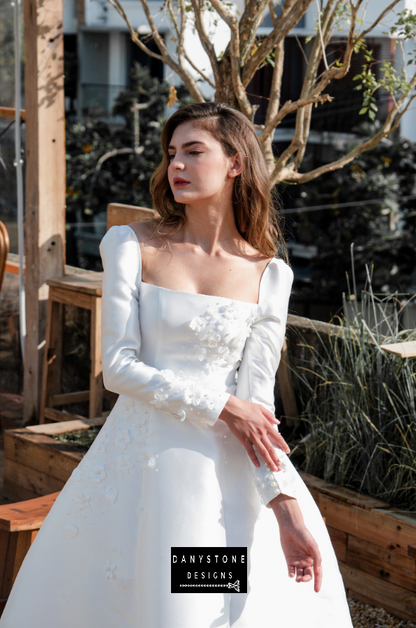 Model posing in a greenhouse setting wearing the 7-piece tafta dress with embossed flowers and long sleeves.