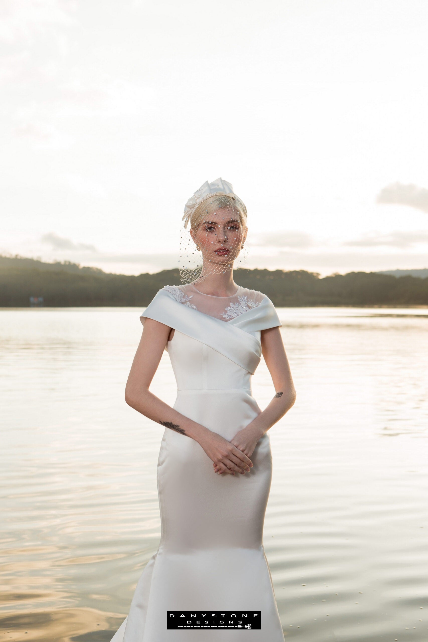 Image 1: Bride wearing a satin mermaid wedding dress with floral appliqué, standing by a serene lake.