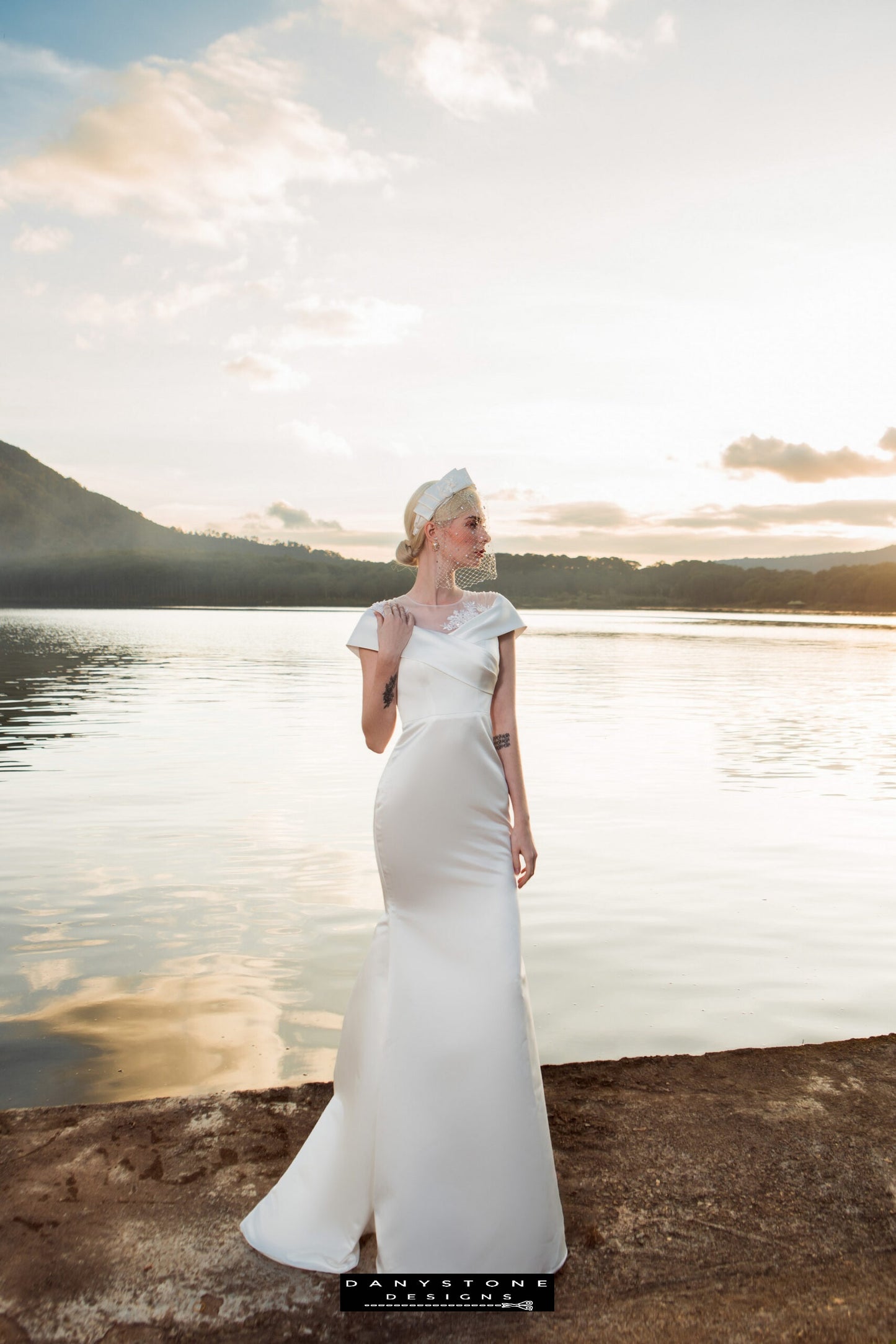 Image 2: Side view of a bride in a satin mermaid wedding dress with floral appliqué, lakeside at sunset.