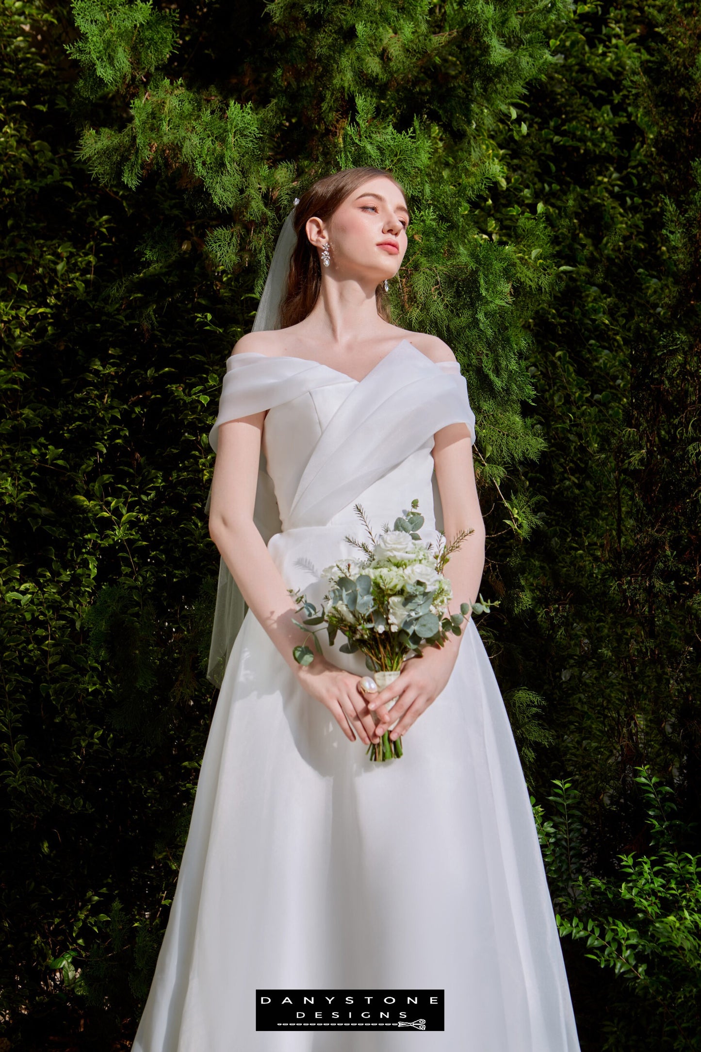 Classic Off-the-Shoulder Bridal Dress with Bow Detail - Model presenting the side view of the gown, showcasing the elegant pleats and captivating bow at the back.