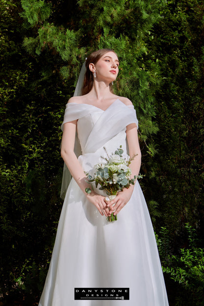 Classic Off-the-Shoulder Bridal Dress with Bow Detail - Model presenting the side view of the gown, showcasing the elegant pleats and captivating bow at the back.