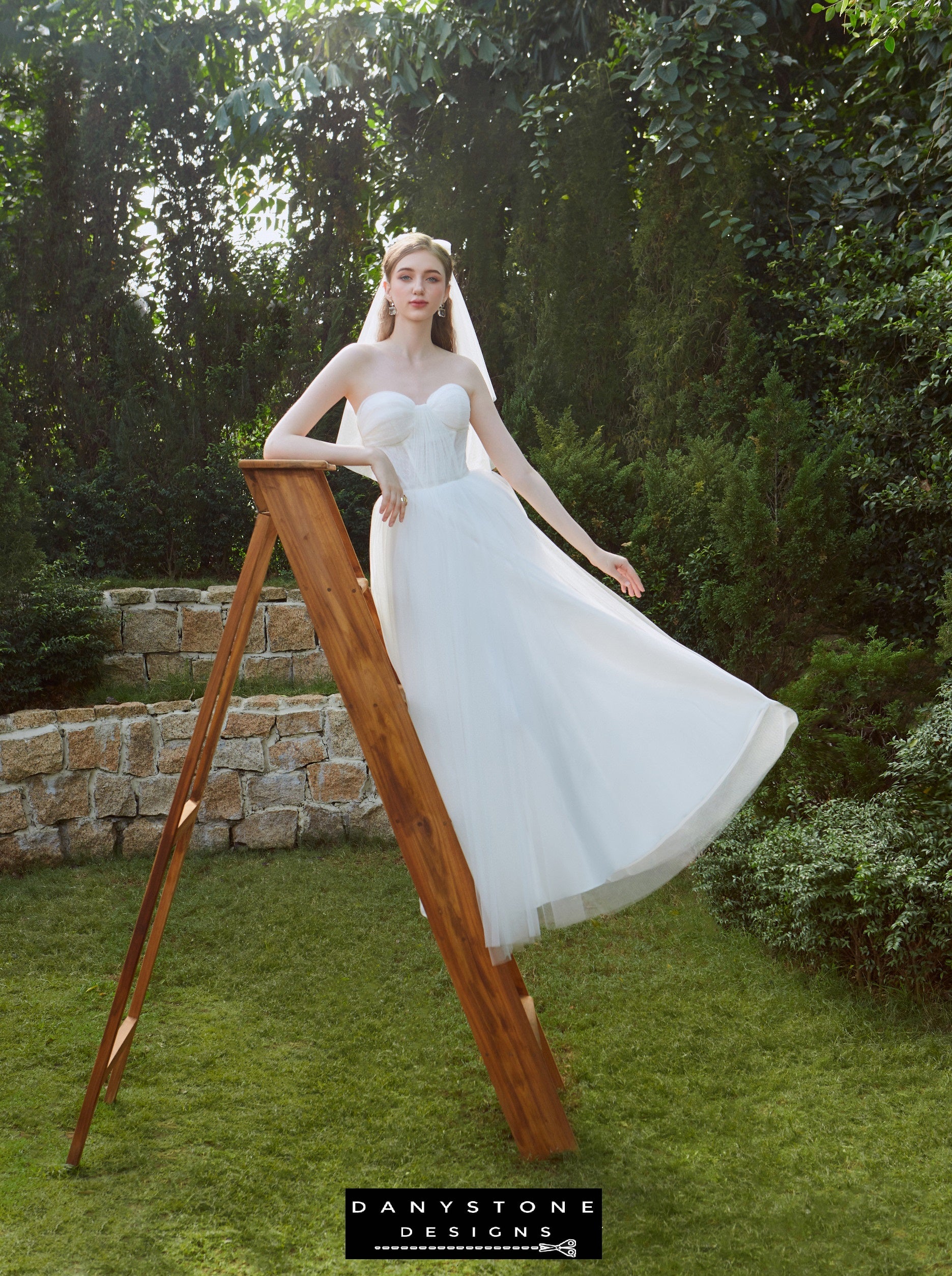 Bride sitting in garden wearing strapless wedding dress with tulle skirt – Danystone Designs