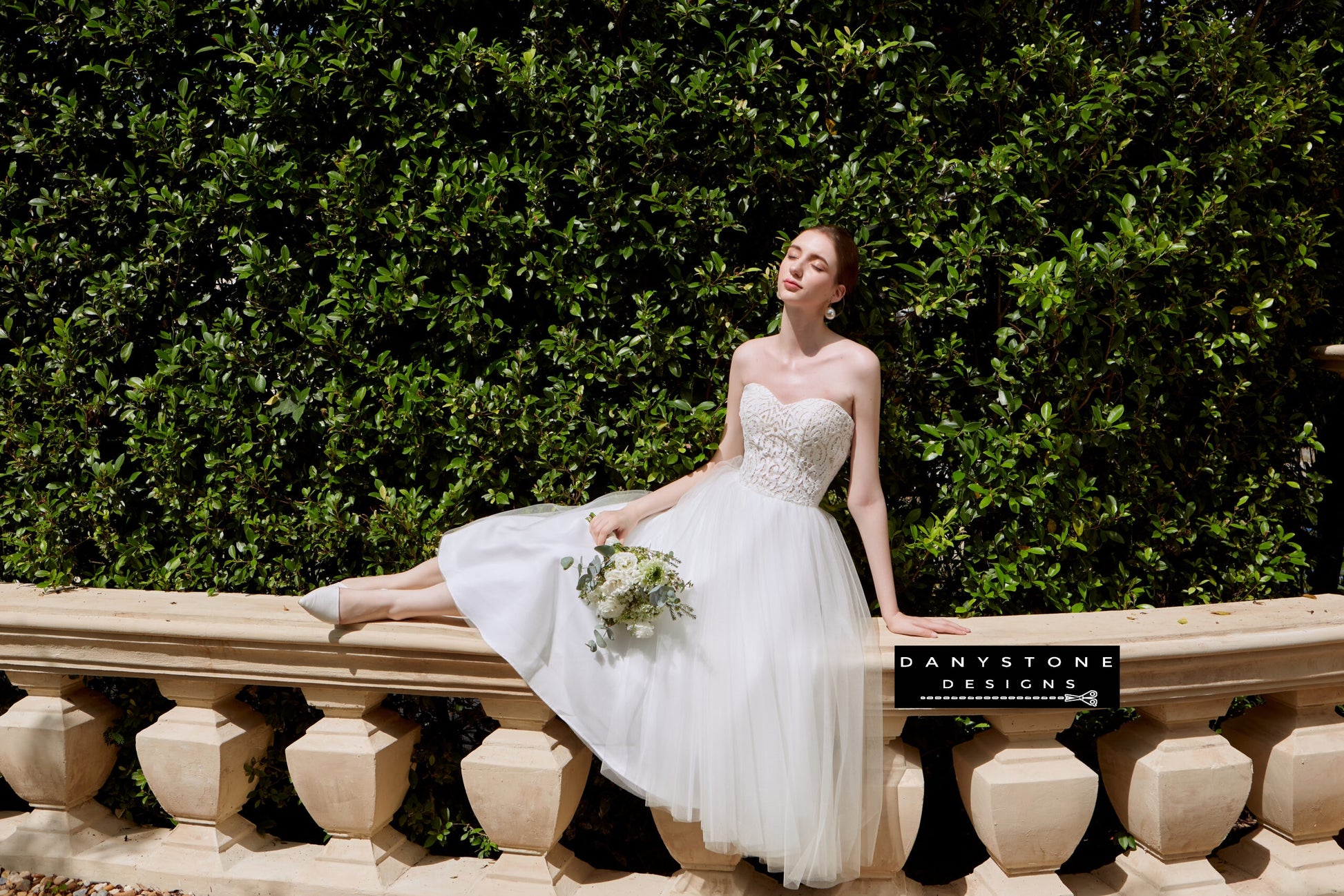 Bride in strapless wedding dress with satin vest, relaxing on a stone ledge.