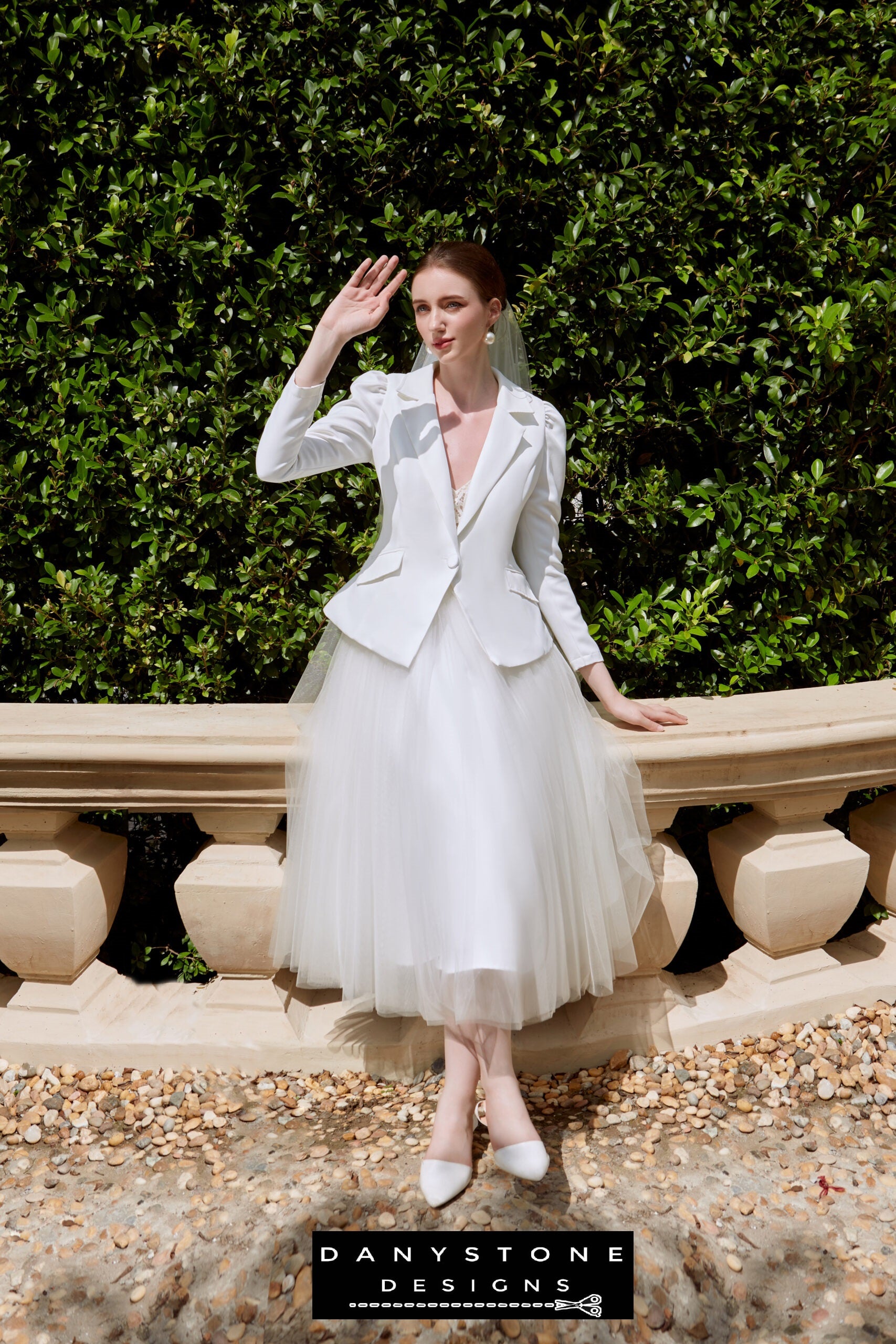 Bride in strapless wedding dress with satin vest, front view with hand raised.