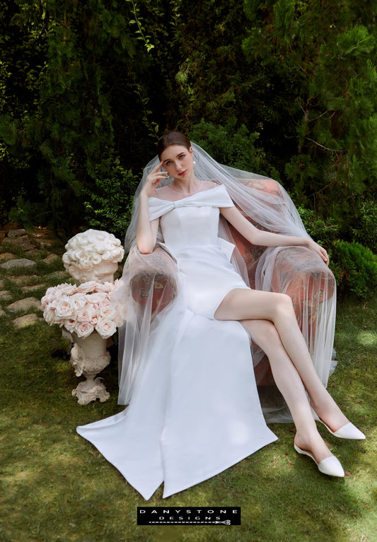 Mini Dress with Flat Shoulders - Elegant Pose - Model sitting elegantly in a garden wearing the mini dress with flat shoulders and a bow back.