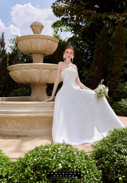 Elegant Bridal Gown with Pearl Trim - Fountain Background - Model posing by a fountain, highlighting the chic strapless design and luxurious tafta fabric of the bridal gown.