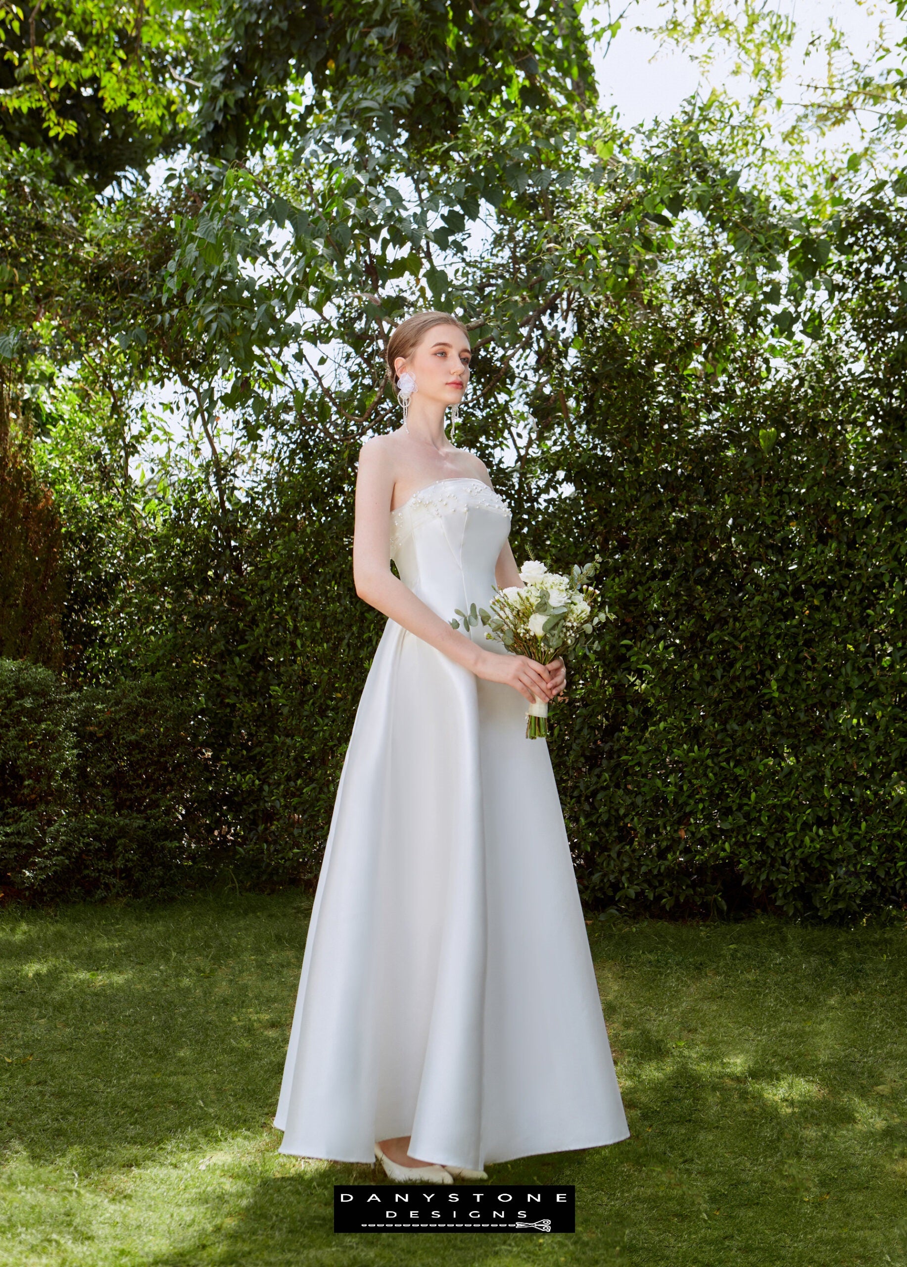 Sophisticated Strapless Wedding Dress - Garden Setting - Model in a garden, presenting the elegant A-line silhouette and pearl mesh trim of the strapless wedding dress.