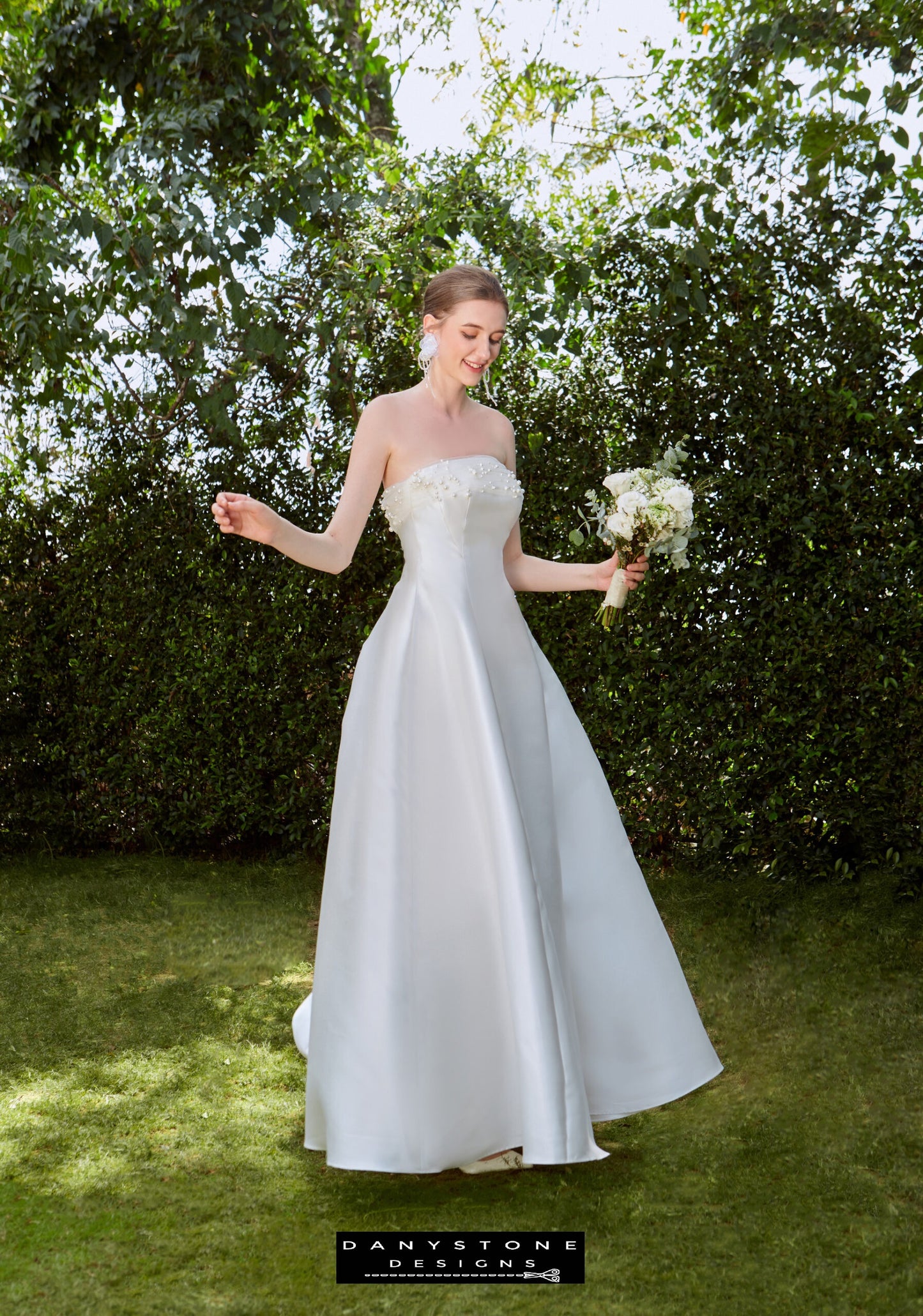 Classic Strapless Bridal Dress with Pearl Details - Model smiling and holding a bouquet, emphasizing the timeless elegance and minimalist design of the dress.