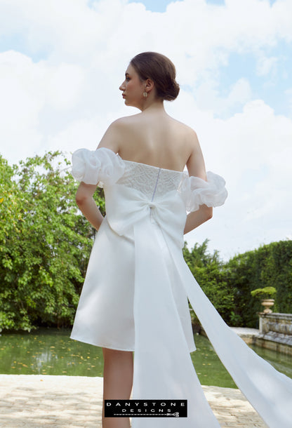 Modern Strapless Bridal Mini Dress - Model standing near a fountain, highlighting the luxurious silk chiffon bow train and the modern mini dress length.