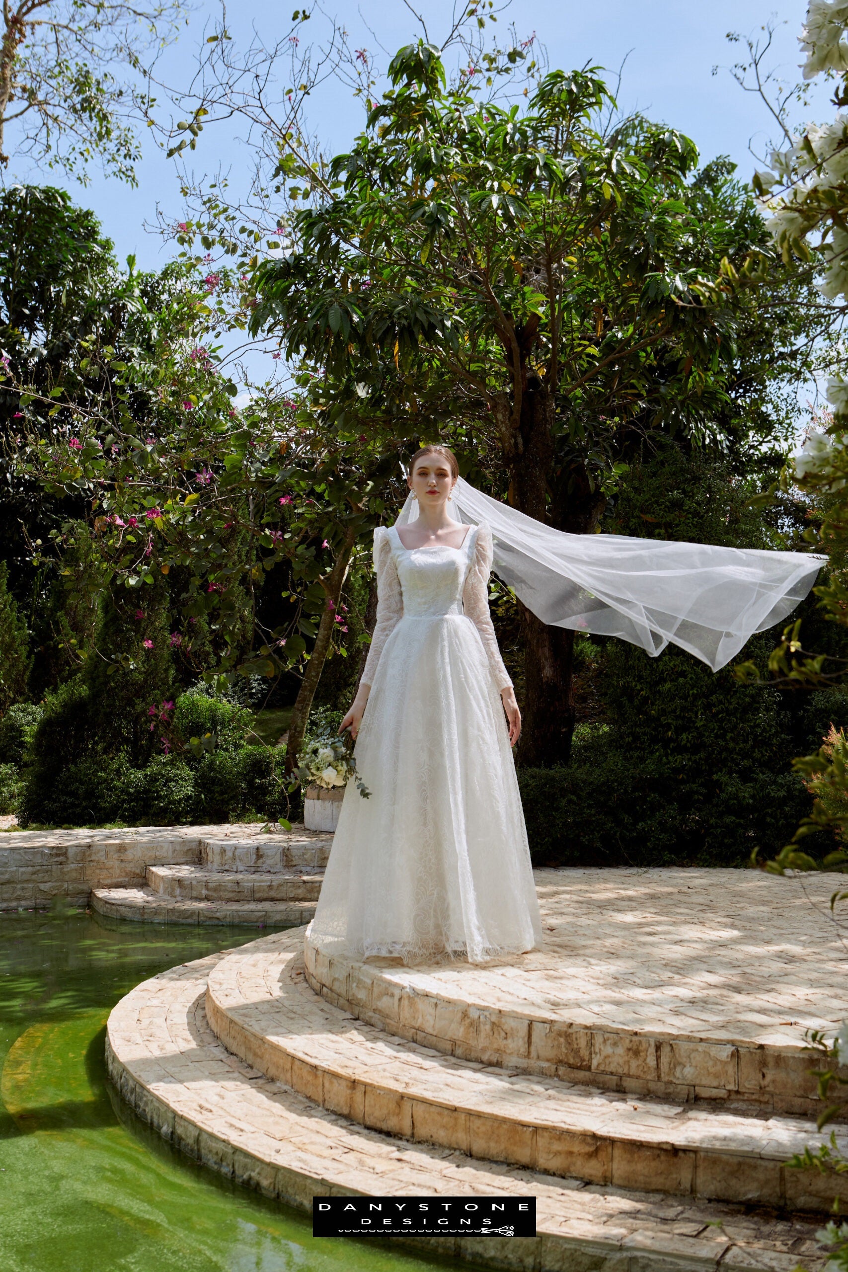 Cinderella Long Sleeve Square Neck Dress - Front View - Model posing in the front view of the Cinderella long sleeve square neck dress with a bouquet, surrounded by lush greenery.