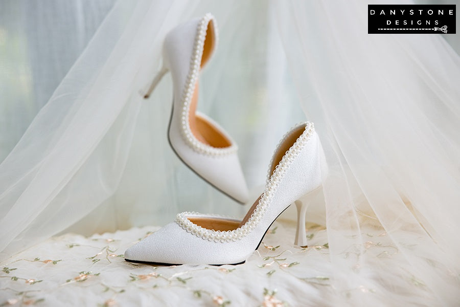 Elegant wedding shoes with pearl trim, made from metallic scratched leather, displayed on a floral fabric.