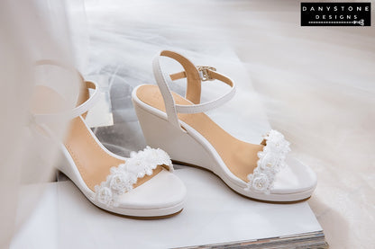 Matte white leather canoe heels with white rose lace trim, displayed on a soft fabric background.