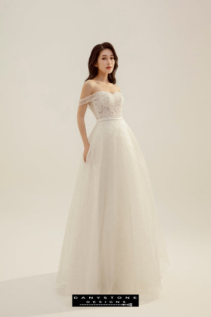 Romantic Flat Shoulder Wedding Dress - Model standing gracefully, showcasing the flat shoulder dress with puffy flowers and subtle sequin embellishments.