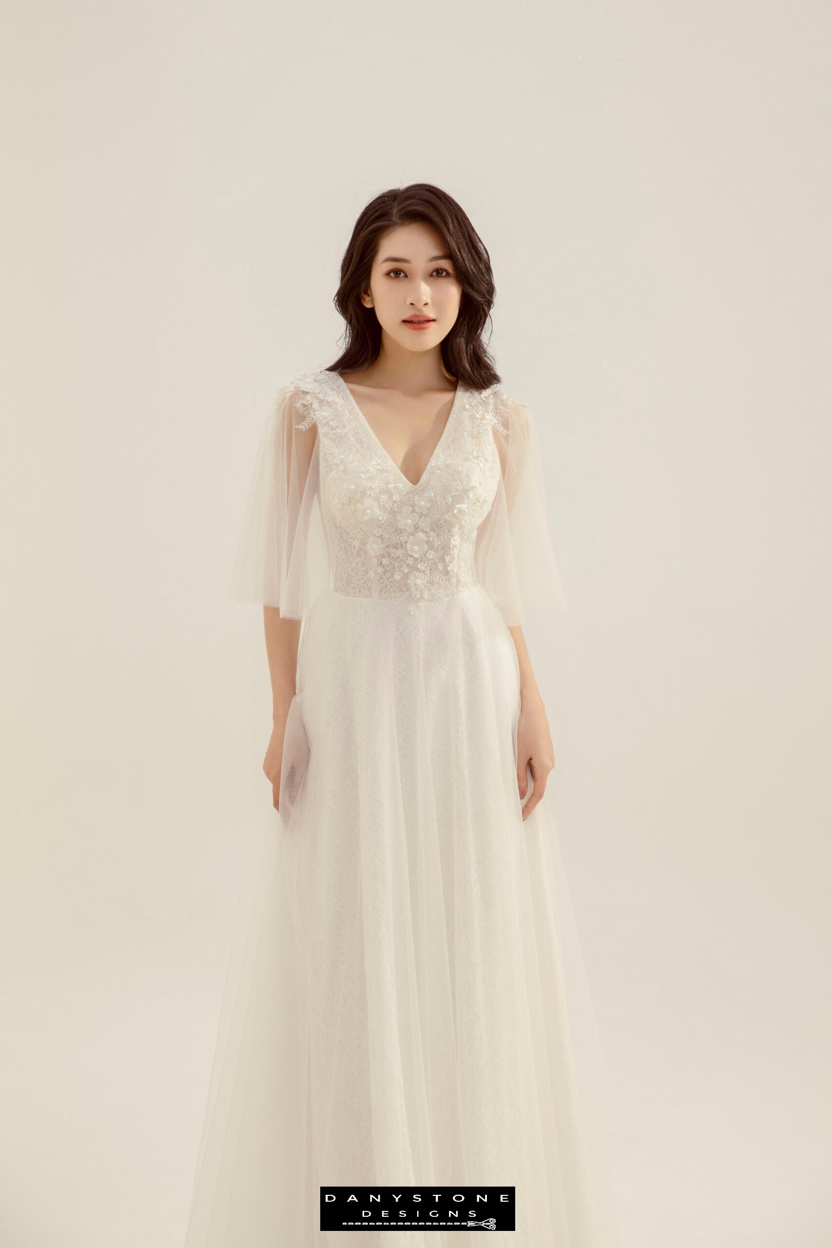 Bride wearing a lace wedding dress with heart collar and fairy petals, standing in a studio.