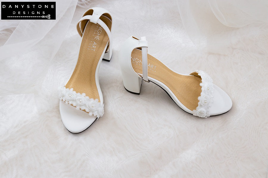 Matte white leather heels with white rose lace trim, displayed on a book with soft fabric.