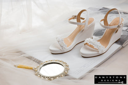 Elegant matte white leather canoe heels with white rose lace trim, displayed on an open book.