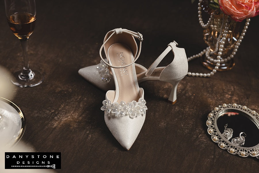 Elegant bridal heels with crystal beaded floral design, displayed with pearls and a vintage mirror.