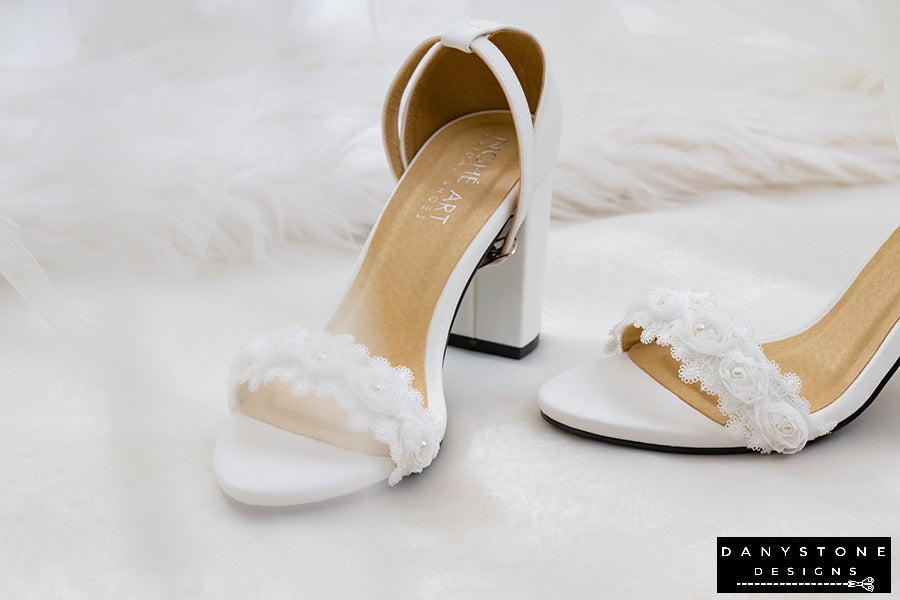 Top view of matte white leather heels with white rose lace trim, showcasing elegant design.