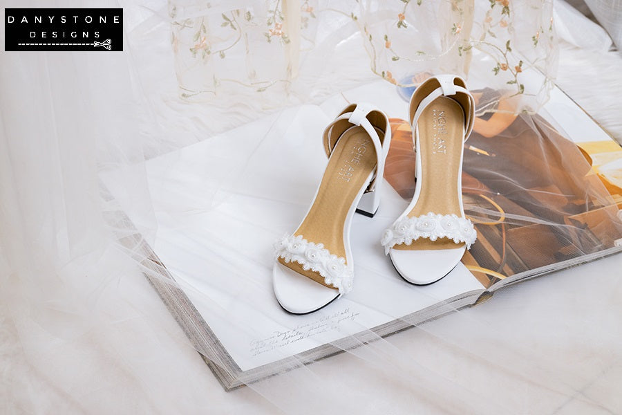 Side view of matte white leather heels with white rose lace trim, featuring block heels.