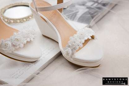 Pair of matte white leather canoe heels with white rose lace trim, displayed with a vintage mirror.