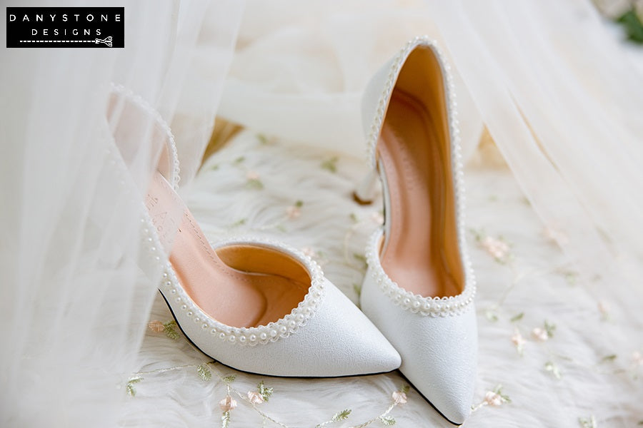 Top view of wedding shoes with pearl trim, displayed on a floral fabric background.