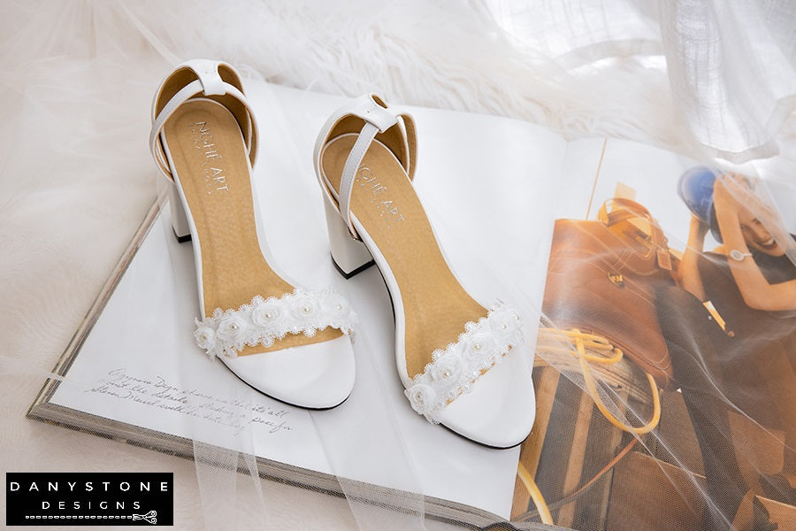 Close-up of matte white leather heels with white rose lace trim, highlighting intricate lace detail.