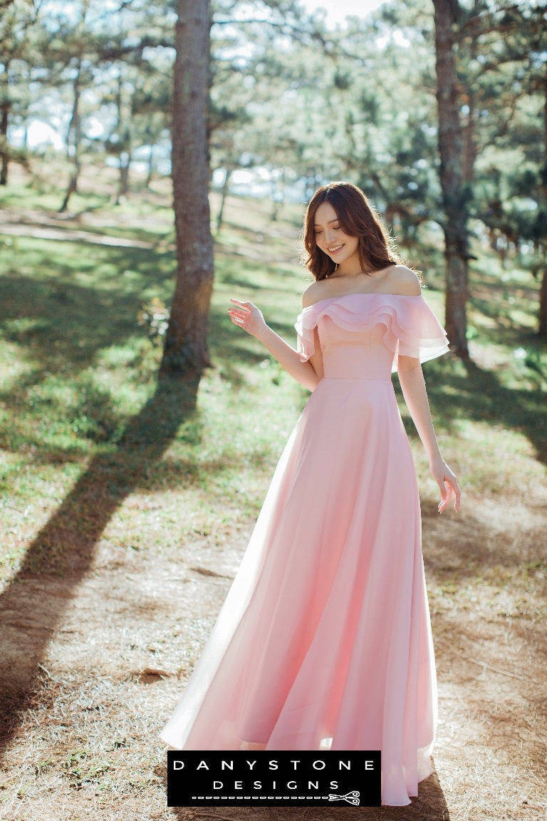 Woman wearing a three-layer off-the-shoulder pink silk chiffon dress standing in a sunlit forest