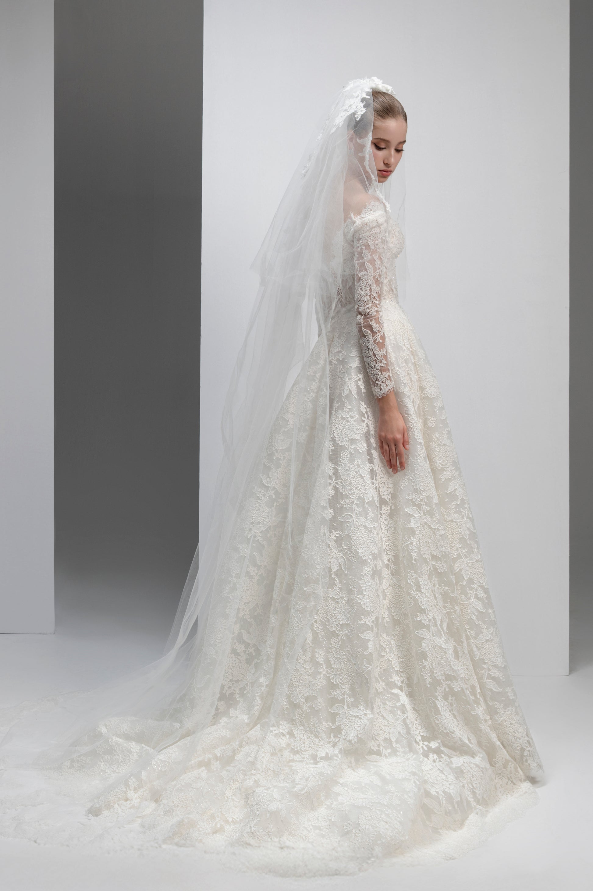 White lace wedding dress with a long veil on a plain background